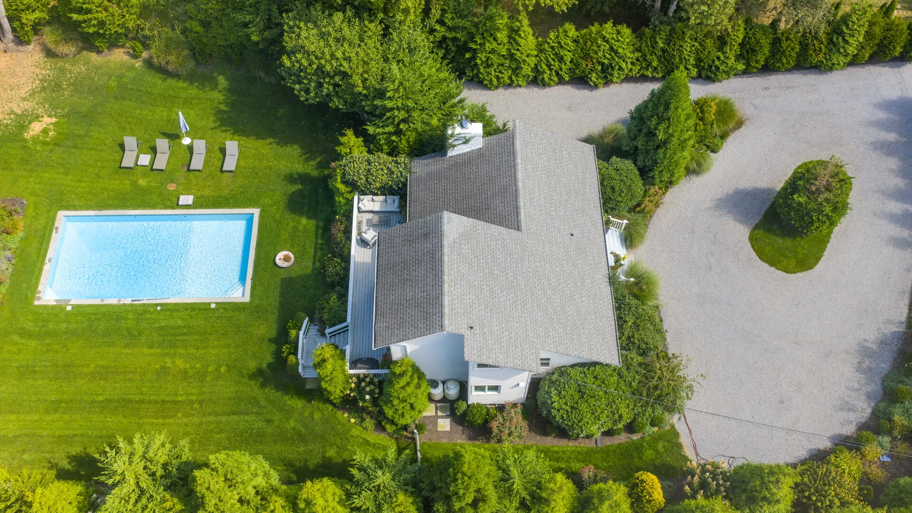 Una vista aérea muestra una casa, una piscina, césped y un camino de grava.