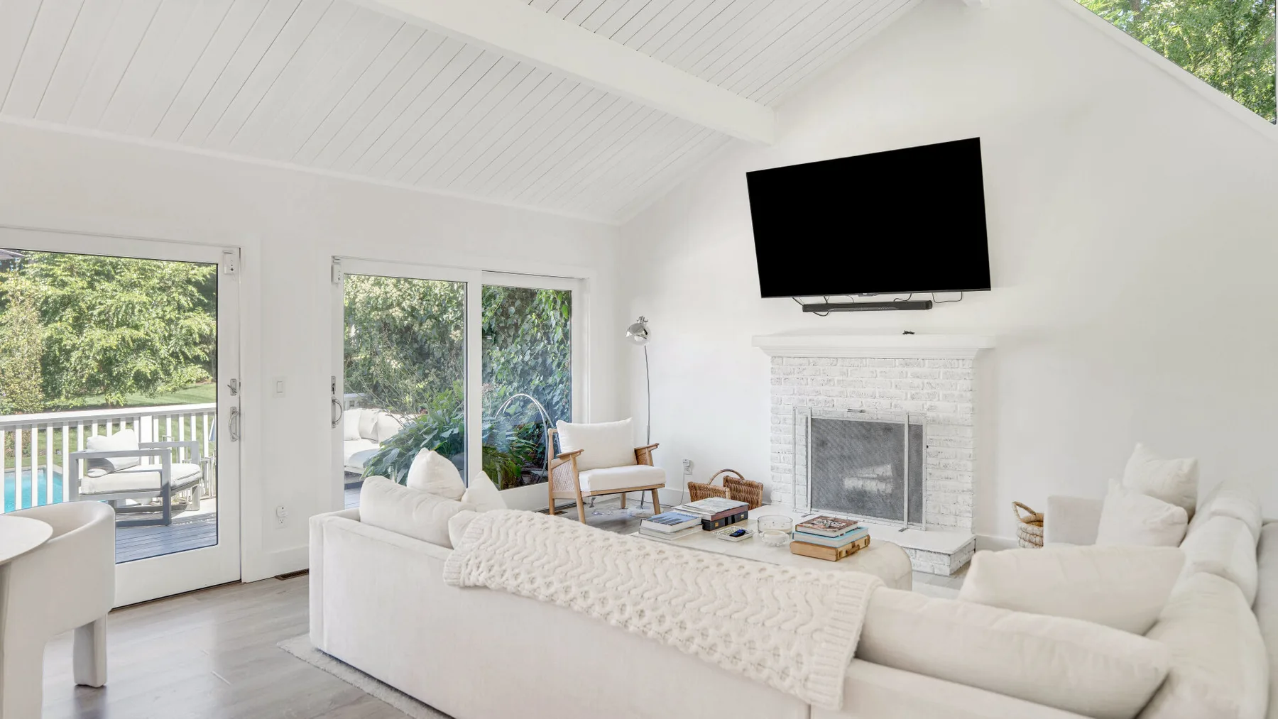 Una luminosa sala de estar con asientos blancos, una chimenea y un televisor en la pared.