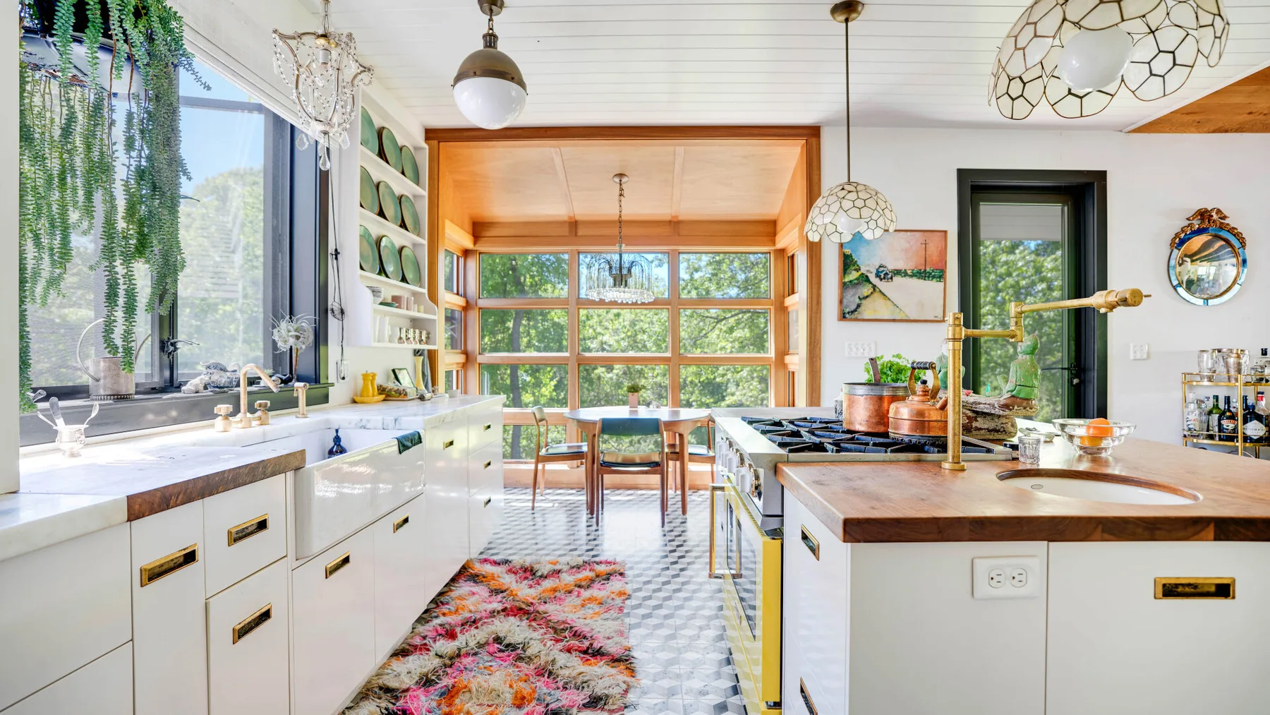 Una cocina luminosa con gabinetes blancos, encimeras de madera y una mesa junto a las ventanas.