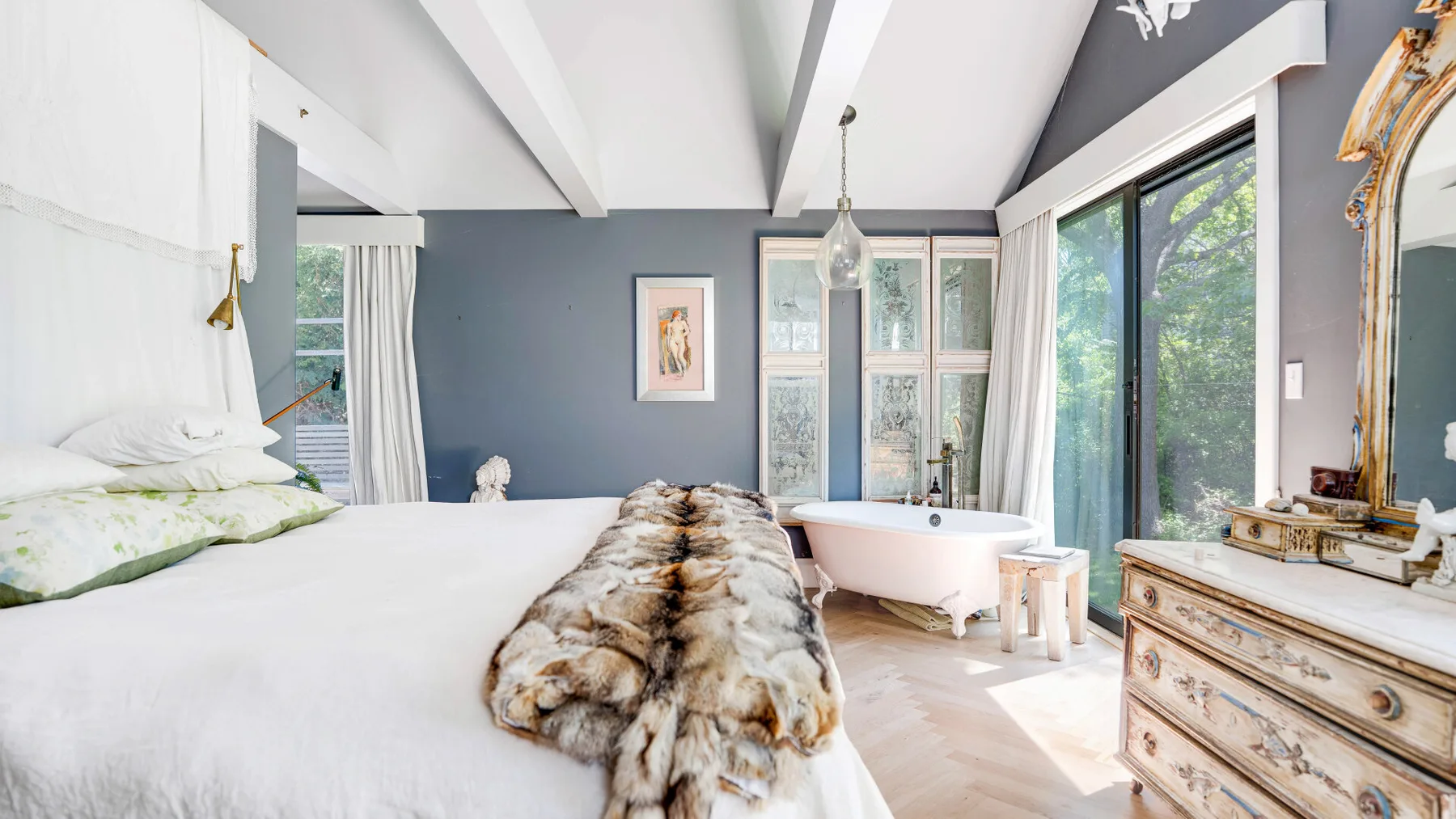 Un dormitorio luminoso con una cama grande, una bañera exenta y ventanas altas.