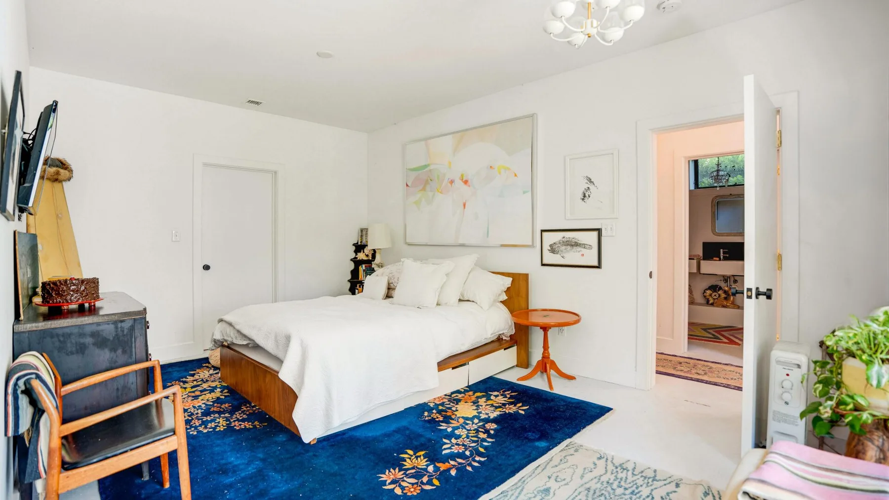 Un dormitorio luminoso con una cama blanca y una alfombra azul floral.