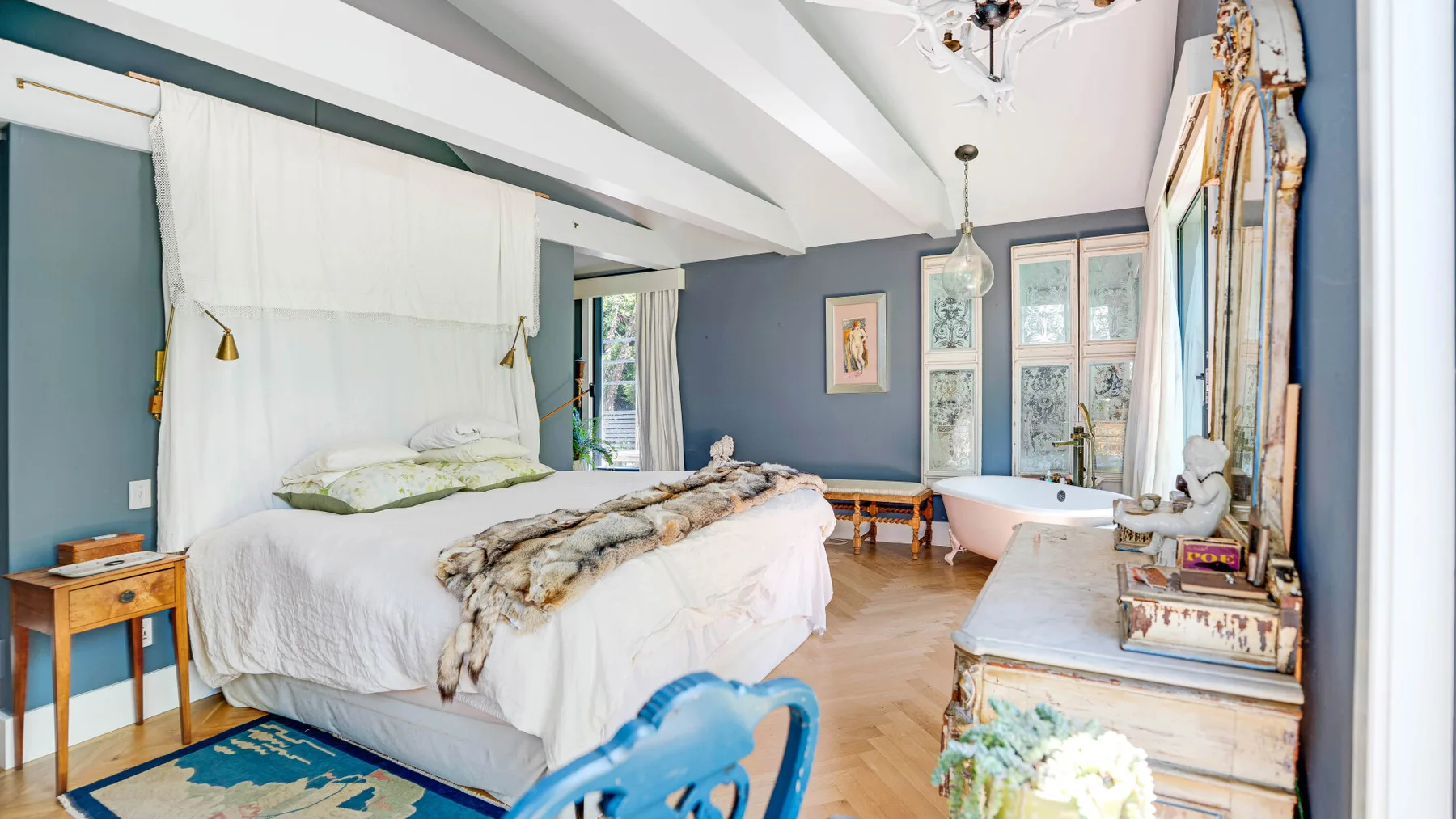 Un dormitorio luminoso con una cama grande y una bañera junto a las ventanas.