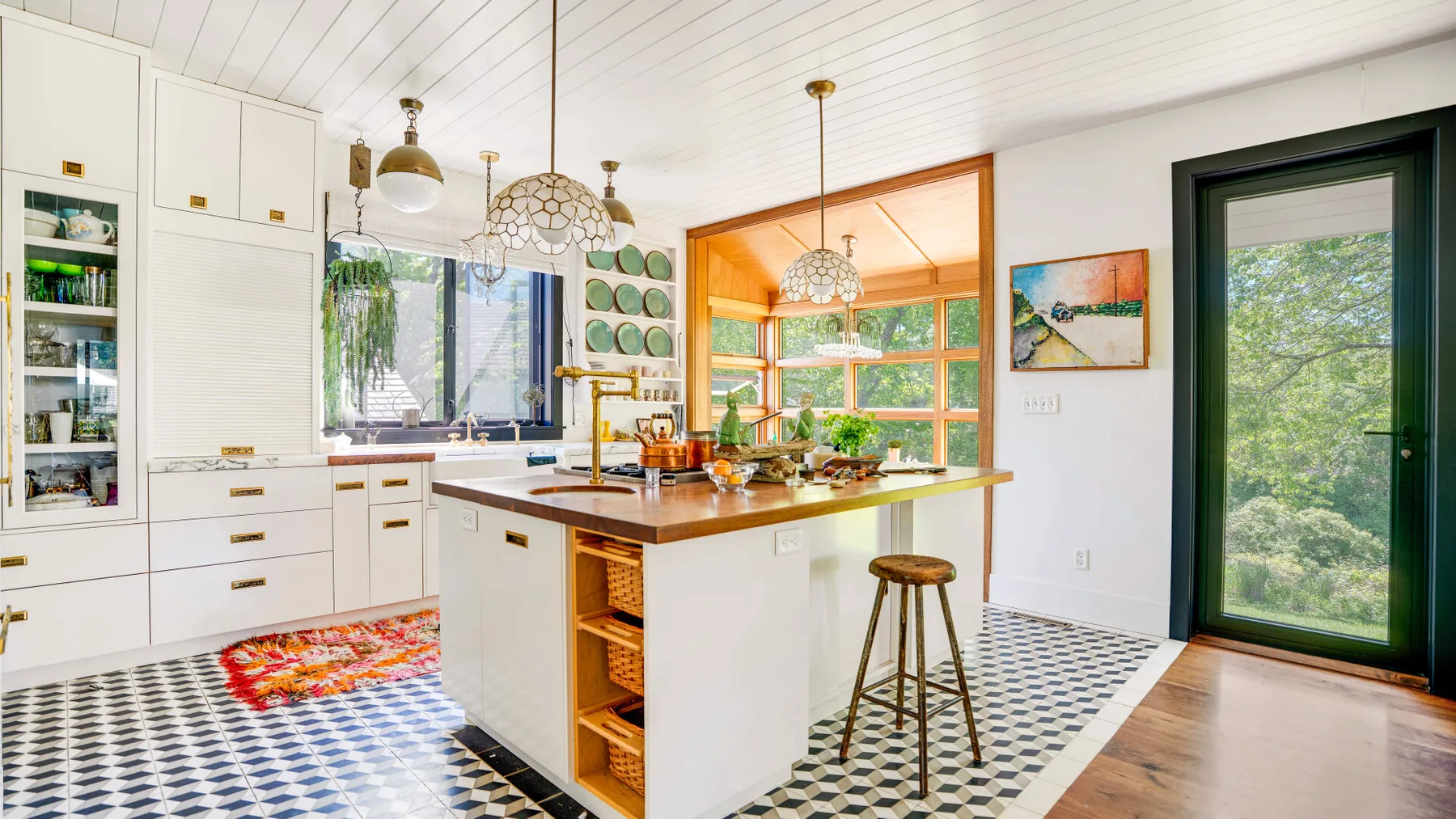 Una cocina luminosa con una isla central, un taburete y ventanas con vistas a la vegetación.