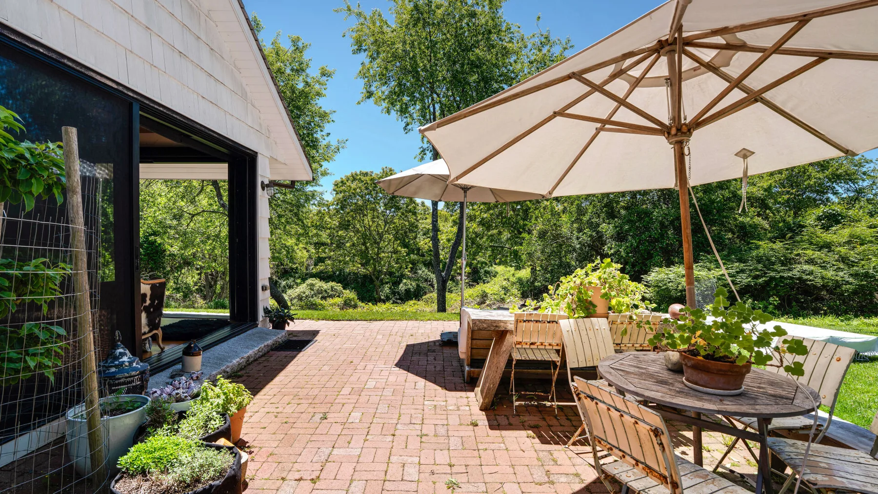 Un patio exterior con una zona pavimentada de ladrillo, asientos y sombrillas grandes.