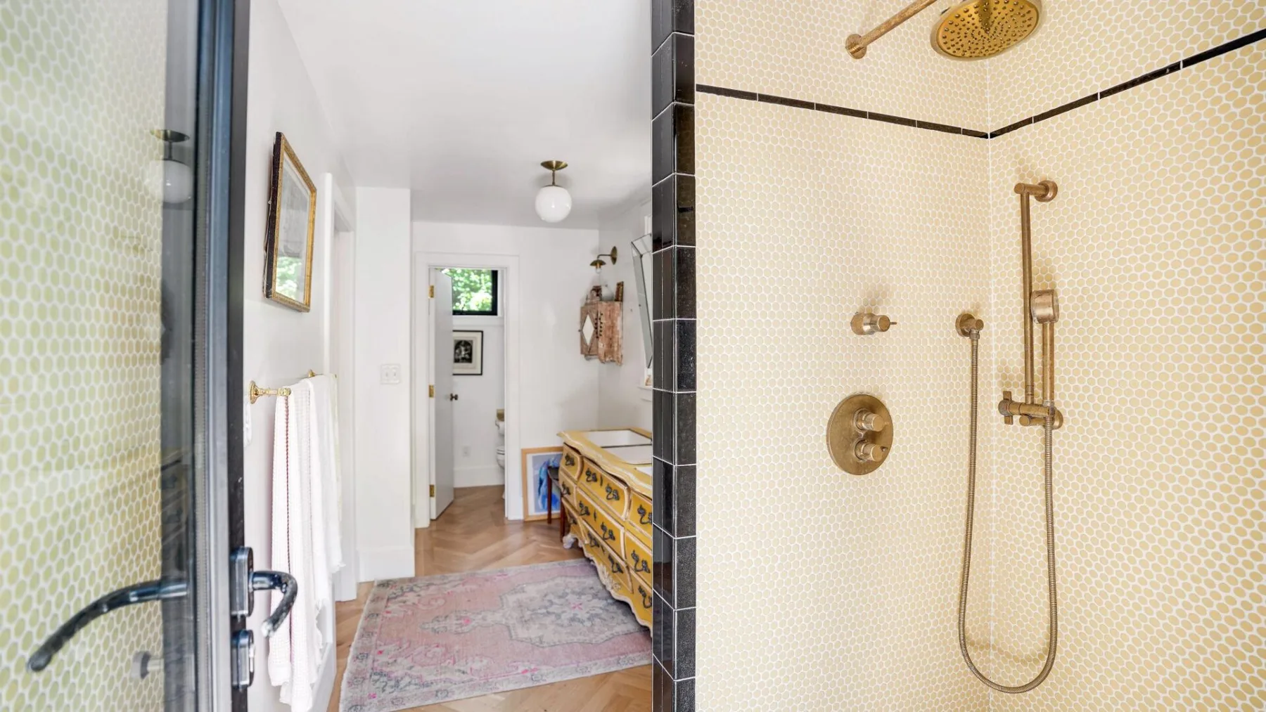 Un baño con una ducha alicatada y una cómoda de madera junto a la puerta.