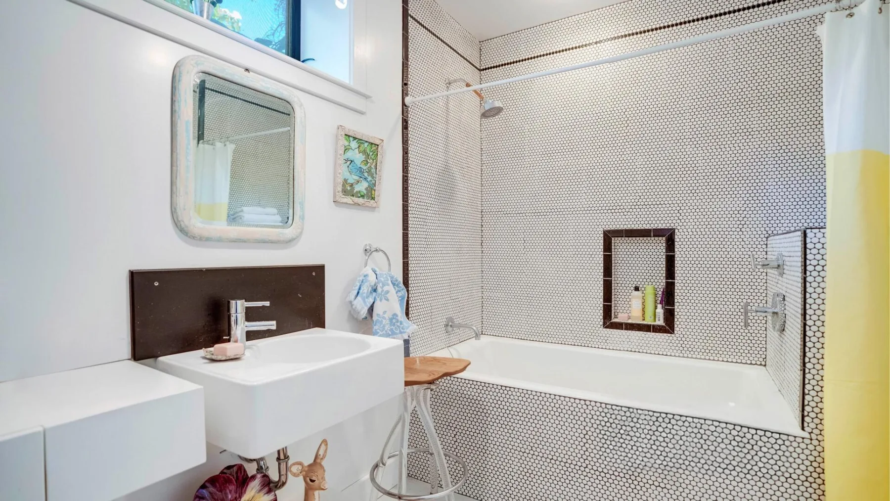 Un baño luminoso con lavabo blanco, espejo y zona de ducha con azulejos.