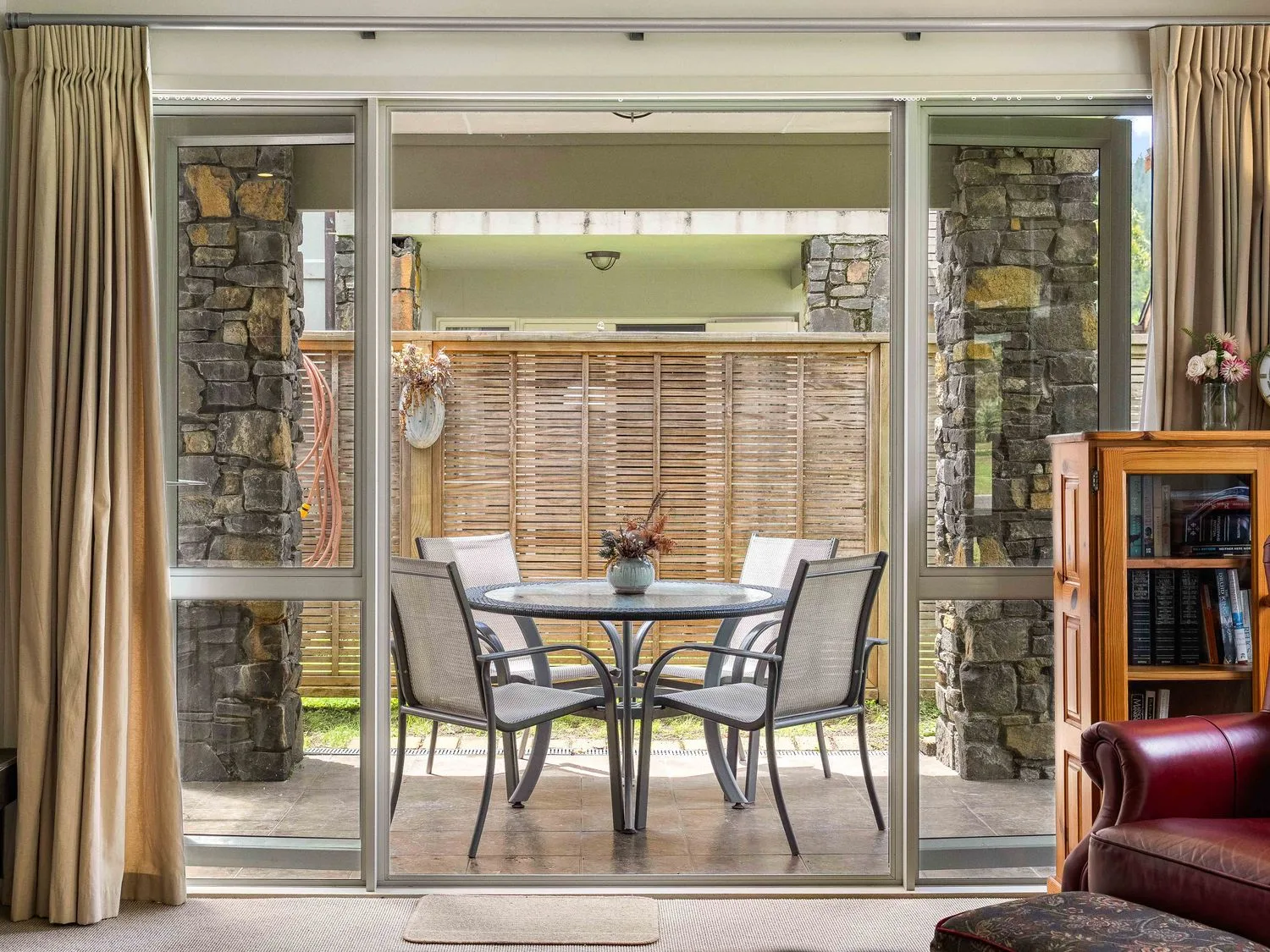 Una zona de estar con vistas a un conjunto de comedor exterior a través de una puerta corredera en Sue's Holiday Home - Pauanui