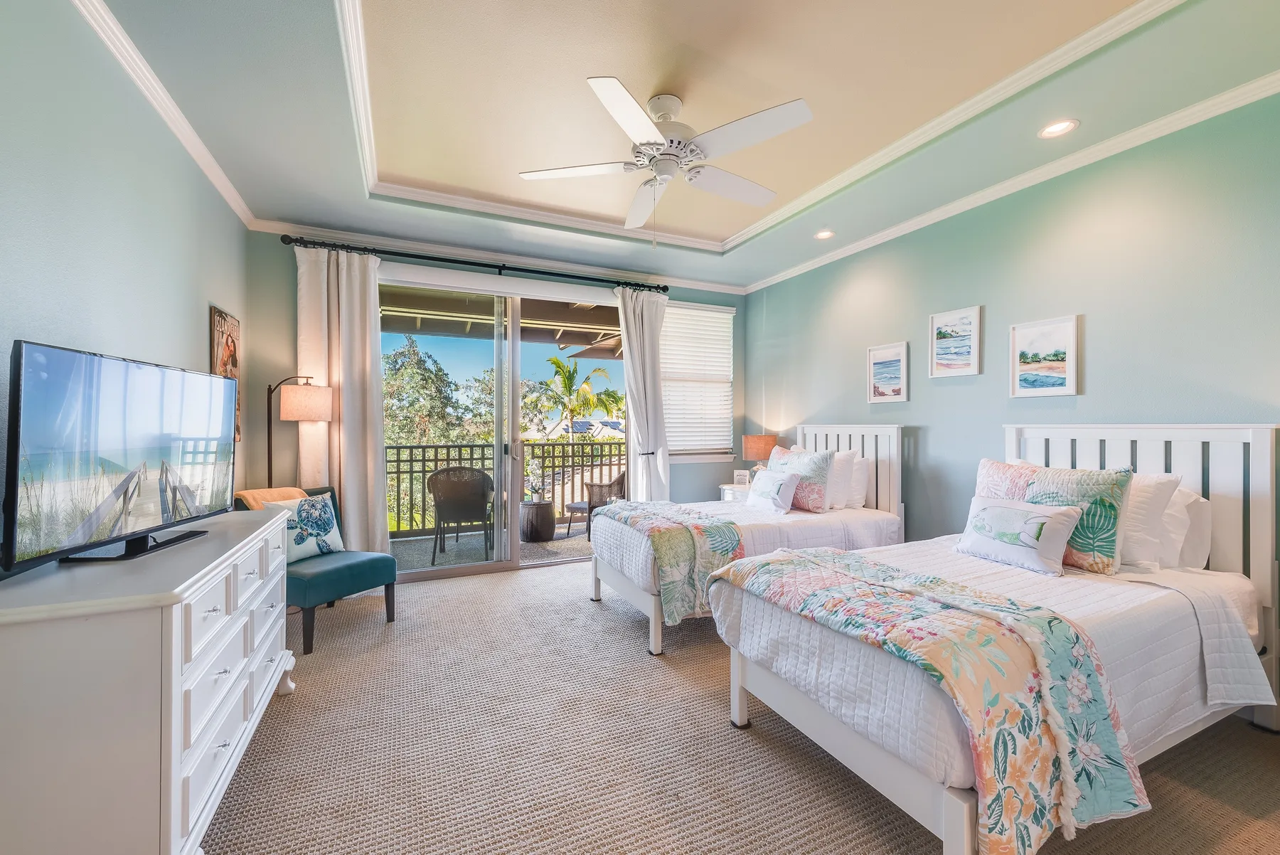 A bright bedroom with two beds, a television, and sliding glass doors to a balcony.
