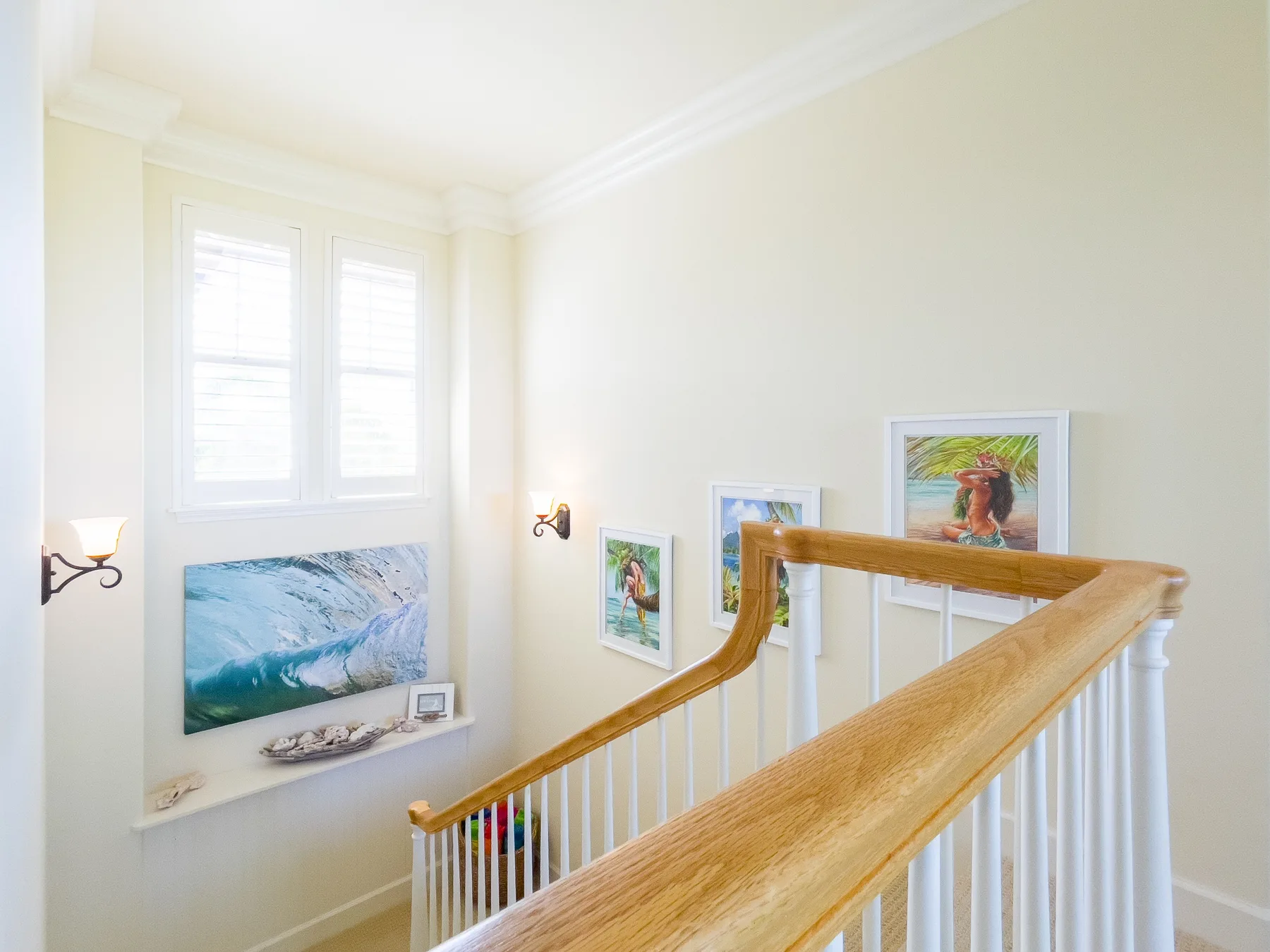A bright stair landing with framed artwork and a wooden handrail.