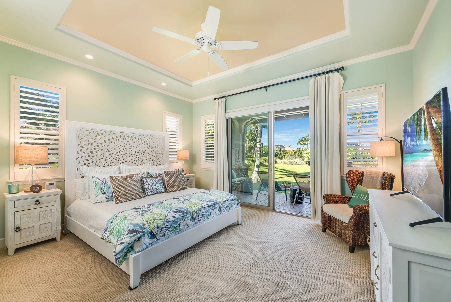 A bright bedroom with a bed, ceiling fan, and sliding glass doors opening to a patio.
