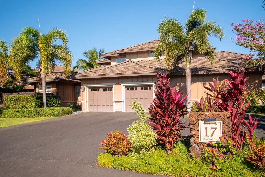 A house with a paved driveway, palm trees, and colorful landscaping.