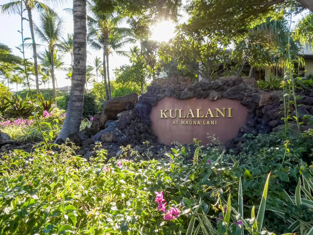 A landscaped tropical garden surrounds a stone entrance sign.