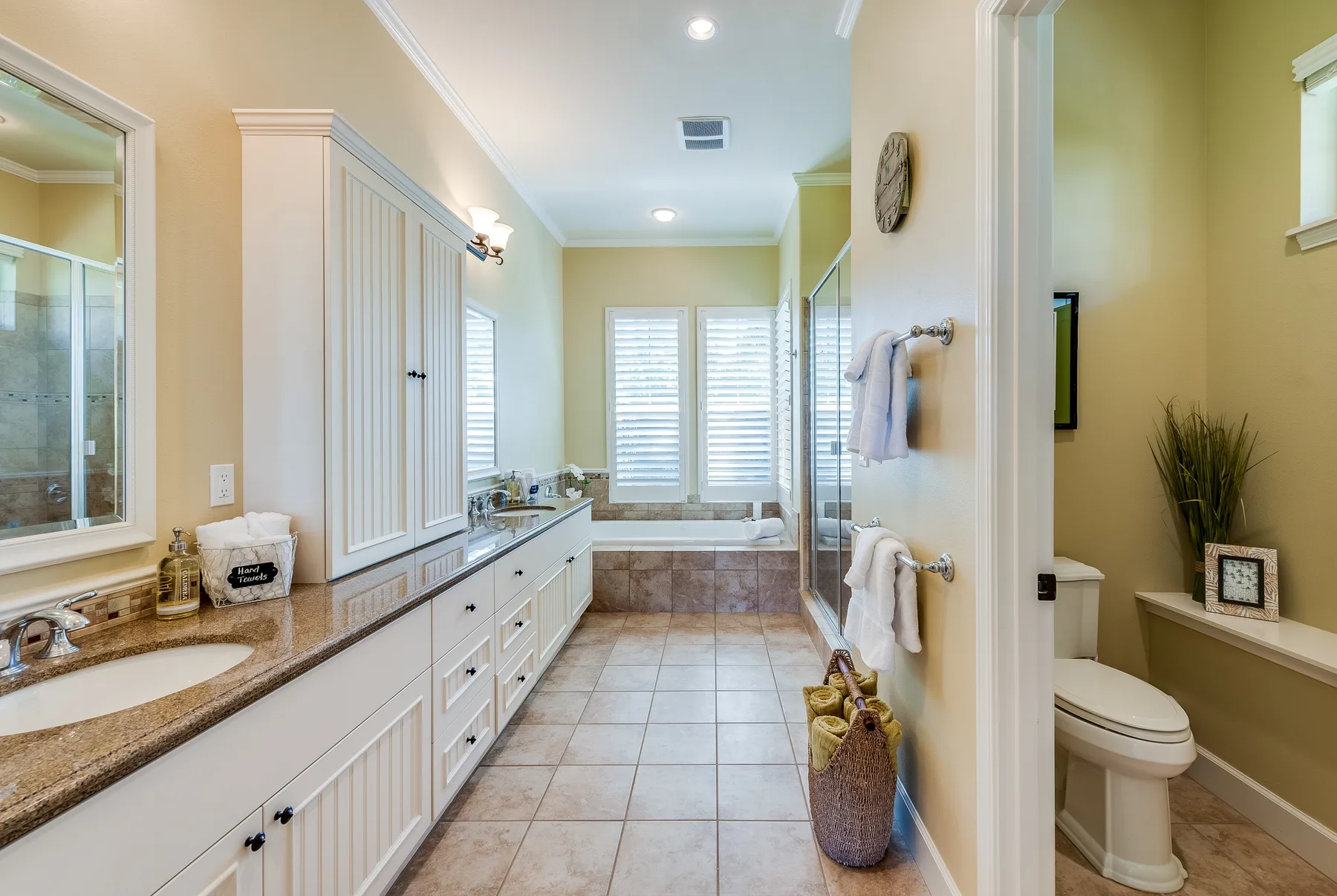 A bright bathroom with a long vanity, bathtub, and shuttered windows.