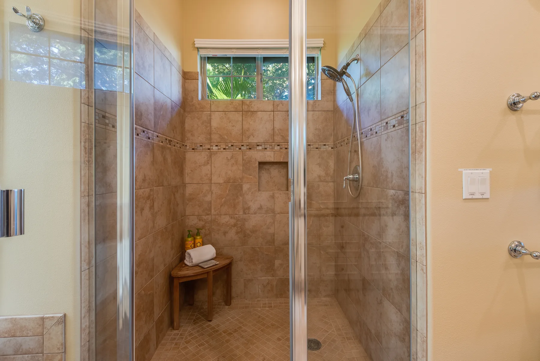A tiled bathroom shower area with a small window and a wooden stool.