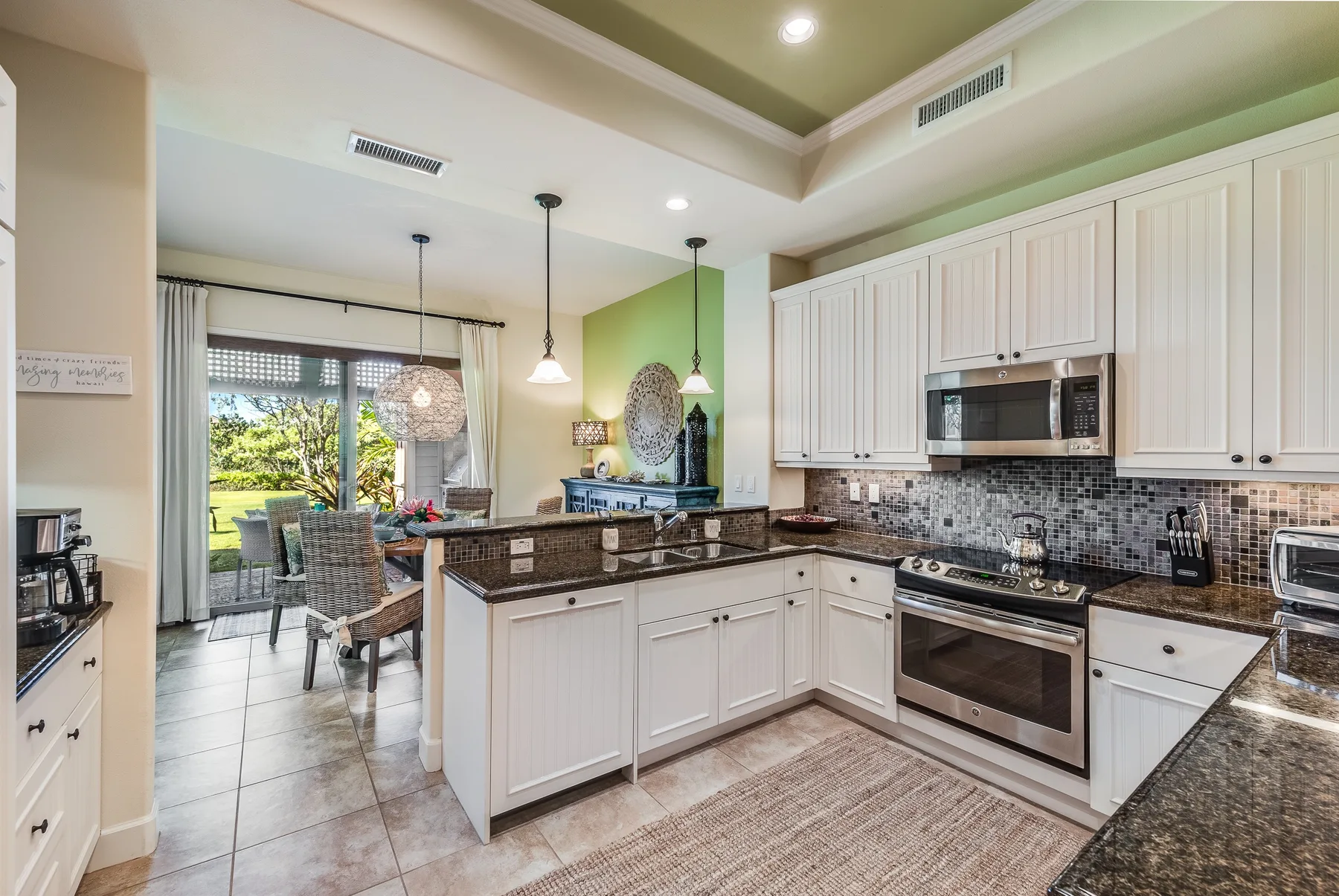 A bright kitchen with white cabinetry, dark countertops, and a dining area by the windows.