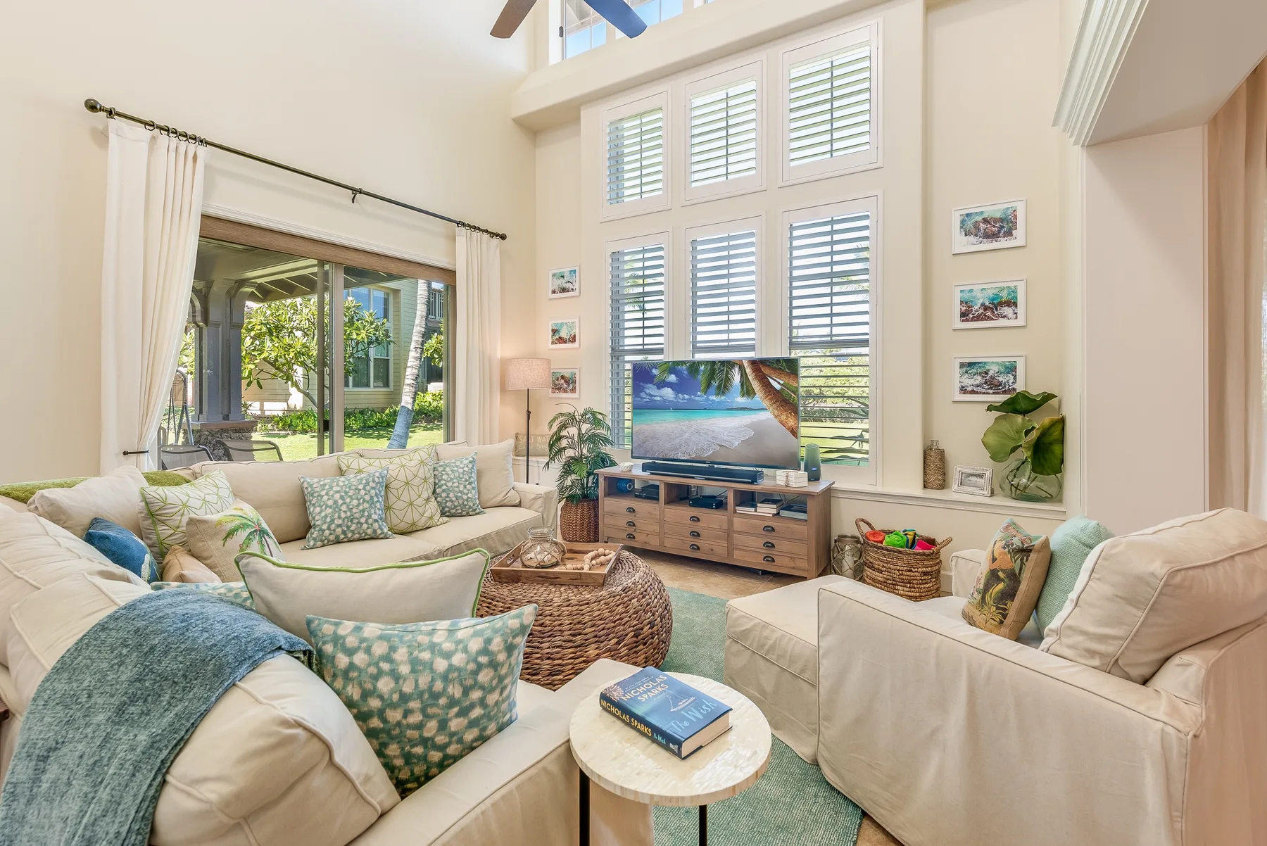 A bright living room with cushioned seating, a television, and tall windows.