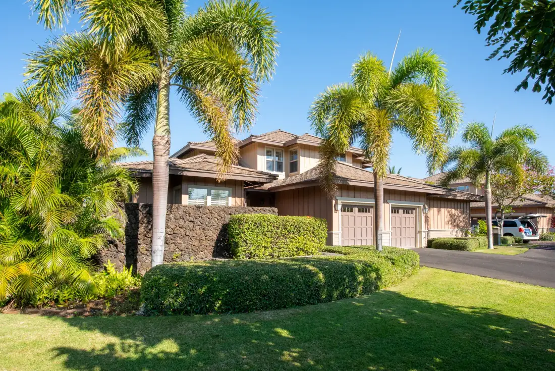 A large house with palm trees and trimmed hedges along the front lawn.