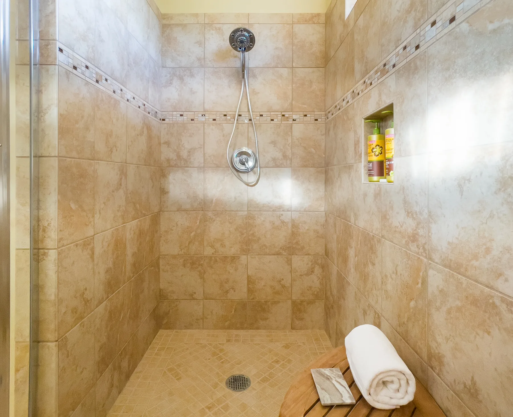 A tiled shower area with a handheld showerhead and toiletries in a wall niche.