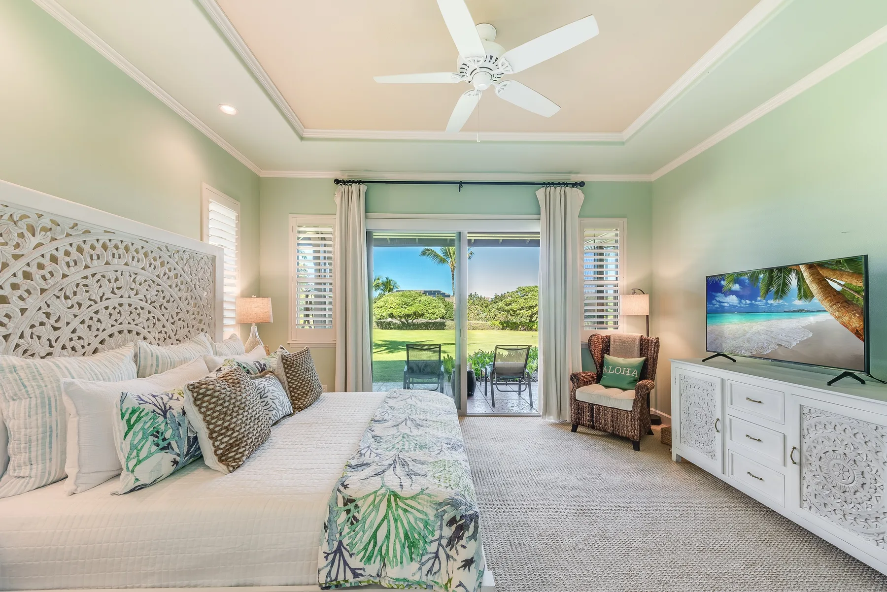 A bright bedroom with a bed facing sliding glass doors and a green outdoor view.