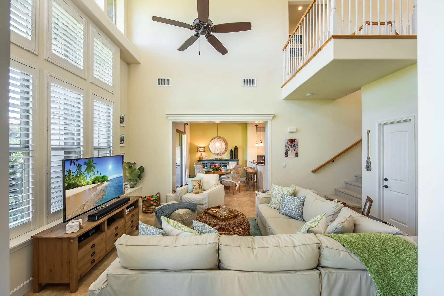 A bright living room with seating, a television, and tall windows with shutters.