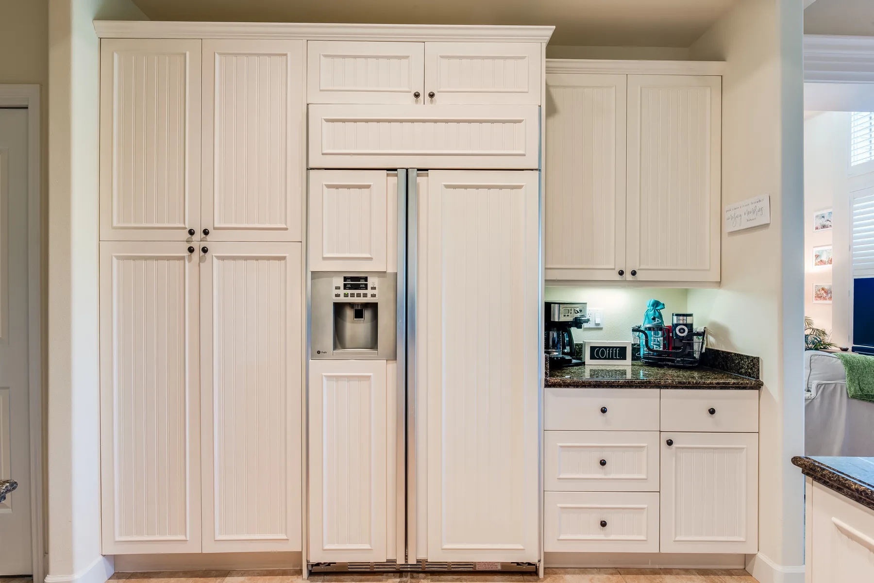 A bright kitchen with white cabinetry, a refrigerator, and a dark countertop.