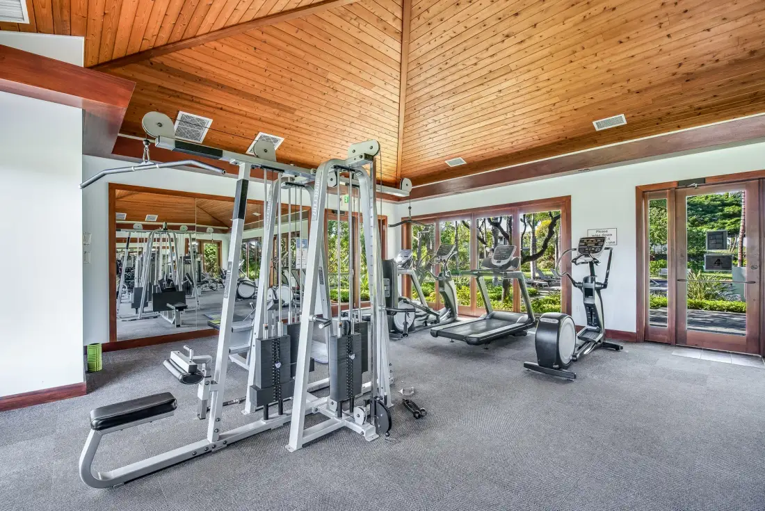 A gym with exercise machines and large windows overlooking greenery.