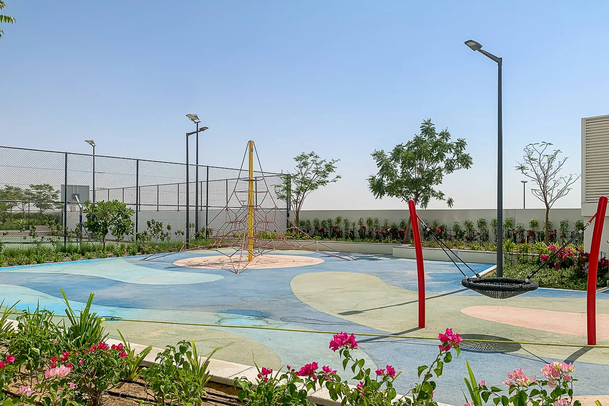 An outdoor play area with colorful ground markings, climbing frames, and landscaped plants.