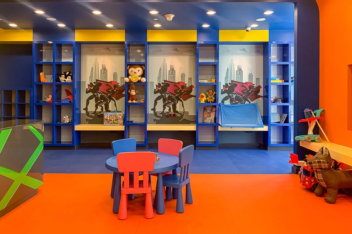 A brightly colored playroom has child-sized seating, toys, and wall shelving.