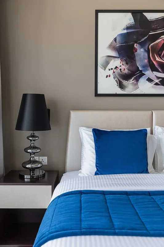 A bedroom with a neatly made bed, blue bedding, and framed wall art.