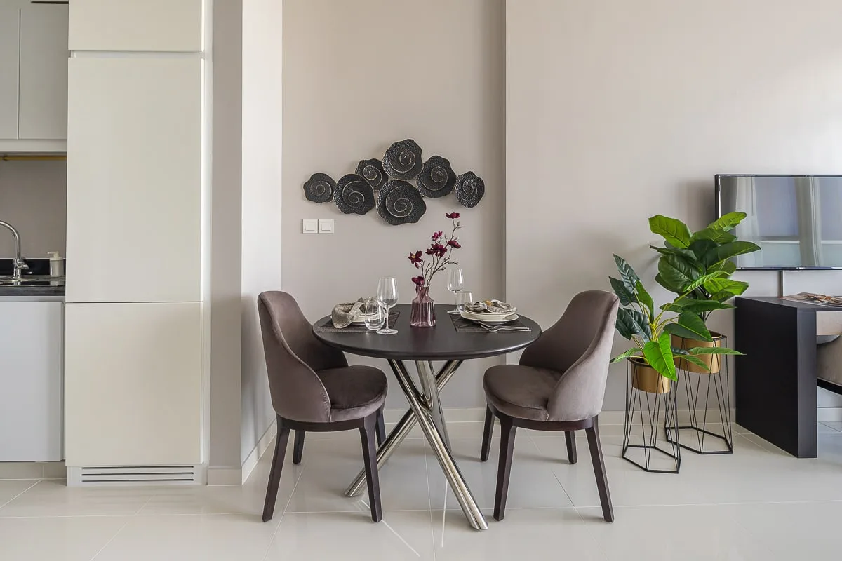 Comedor con una mesa redonda, asientos tapizados y una planta frondosa.