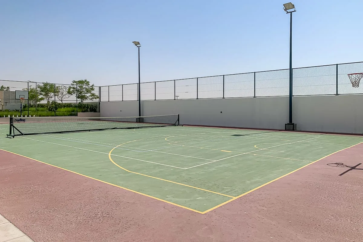 An outdoor sports court with a net, painted lines, and a basketball hoop.