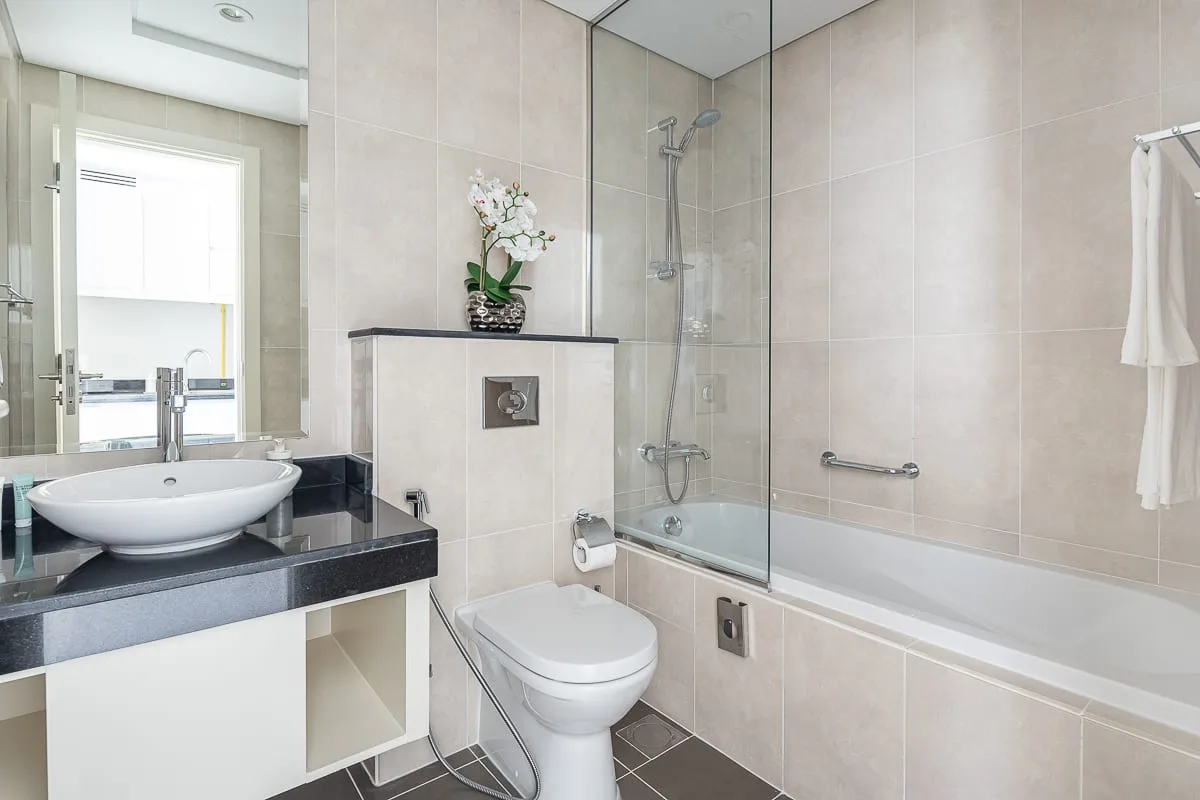 A bright tiled bathroom with a sink, toilet, and bathtub with a shower.