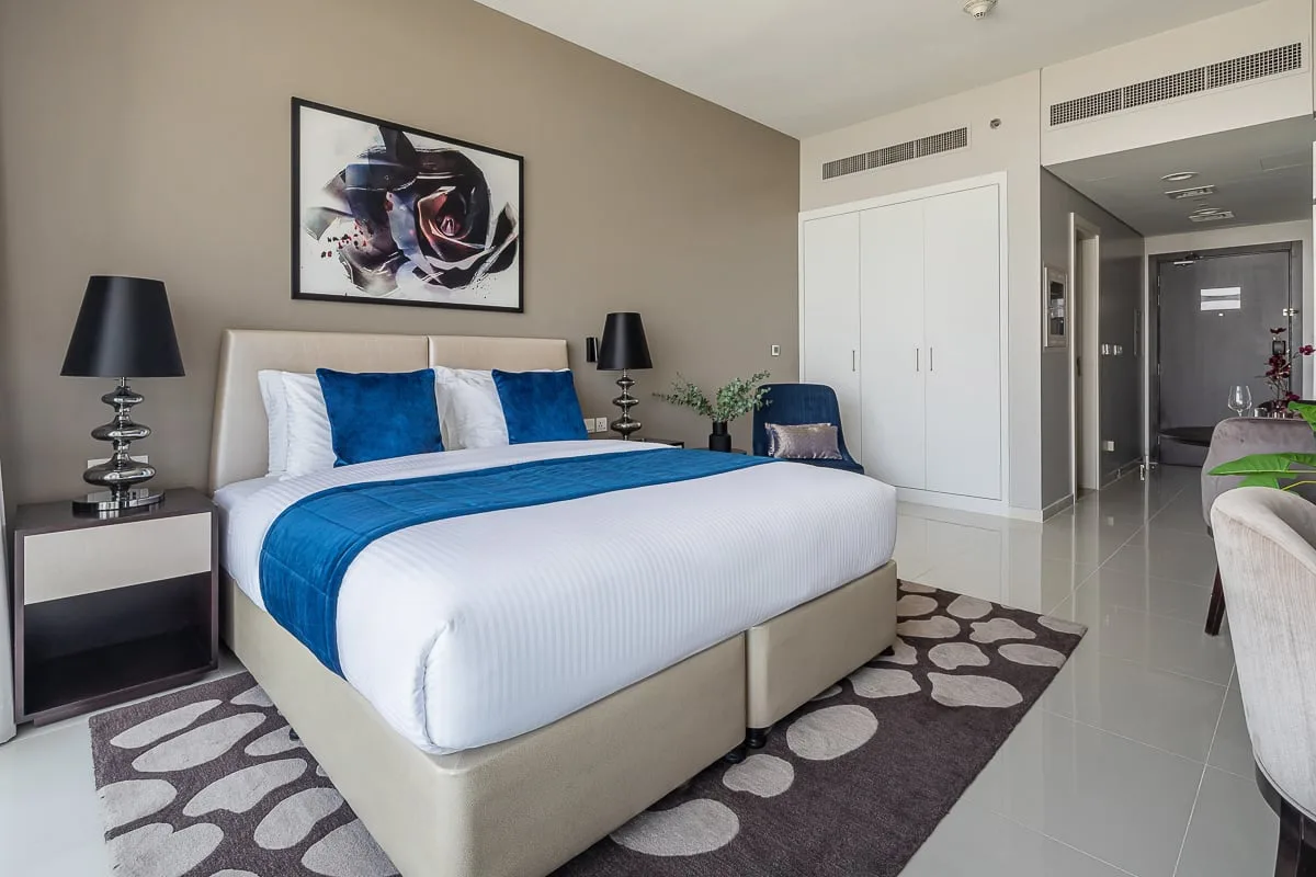 A bedroom with a large bed dressed in white linens and blue accents.
