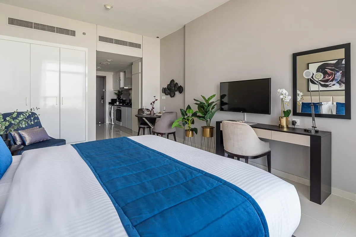 A bedroom with a bed, desk, television, and plants.
