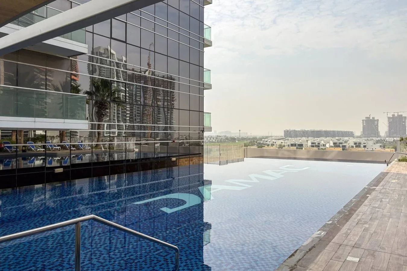 Una piscina en la azotea junto a un edificio moderno de vidrio y una terraza pavimentada.