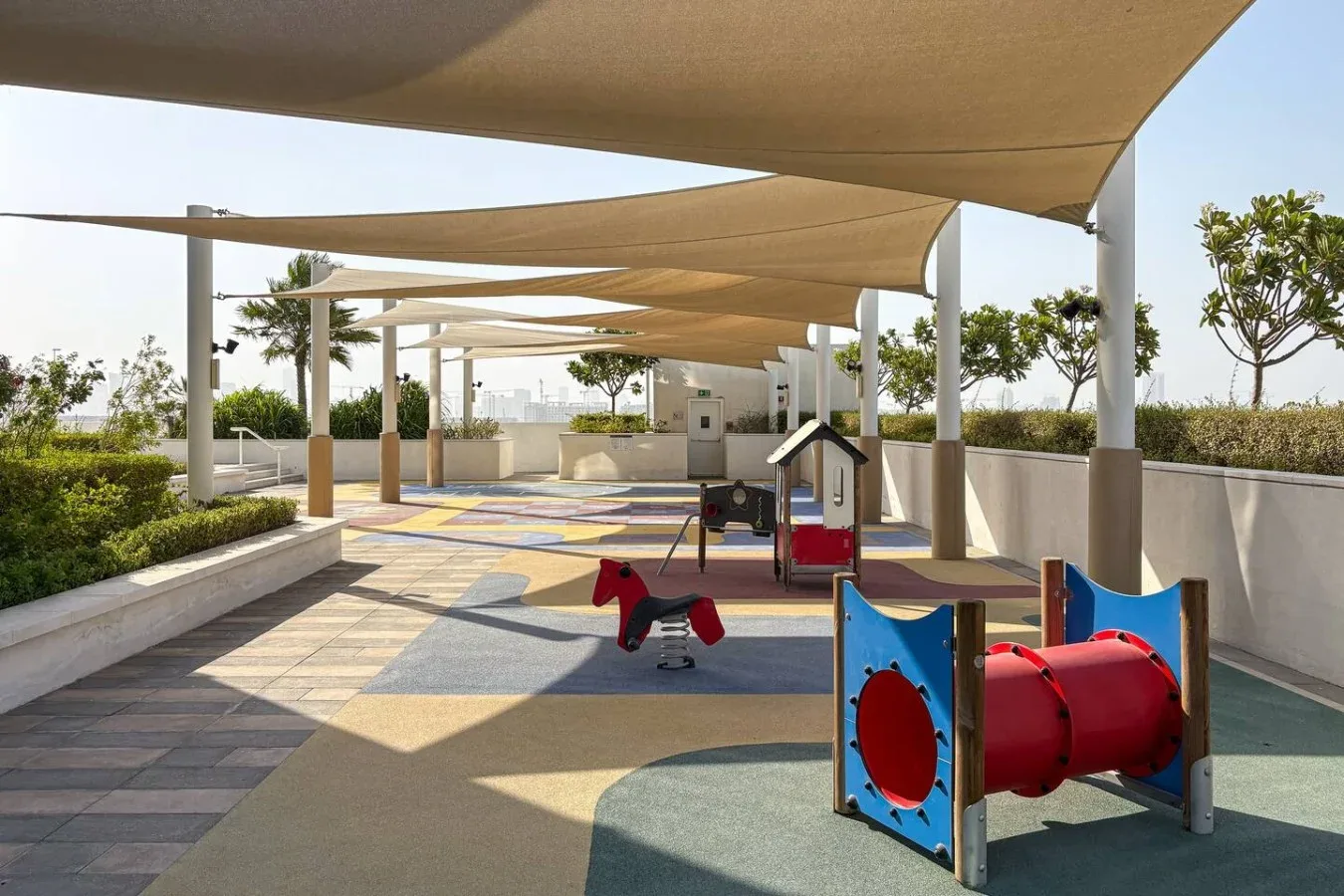 Un parque infantil al aire libre con juegos coloridos y caminos pavimentados, bajo toldos.