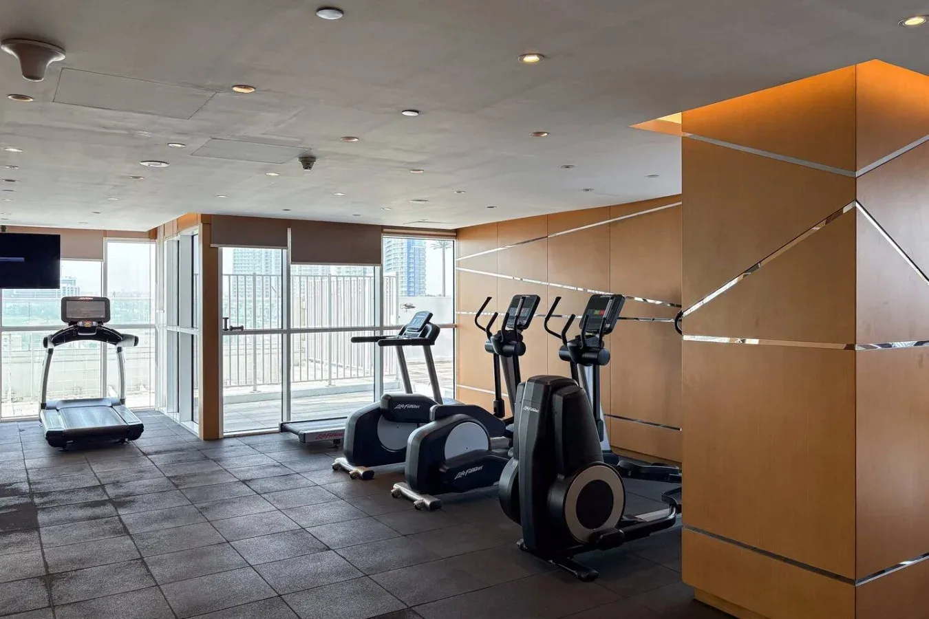 Una sala de ejercicios con máquinas junto a grandes ventanas.
