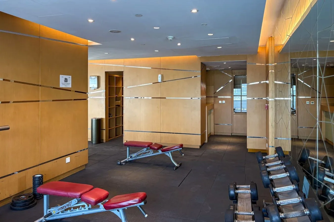 Un gimnasio con bancos de ejercicio y pesas junto a paredes con espejos.