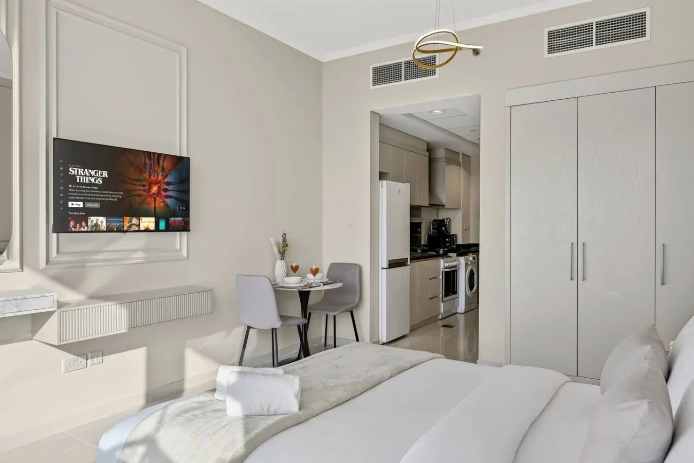 Un dormitorio con una cama, un televisor en la pared y una pequeña zona de comedor.