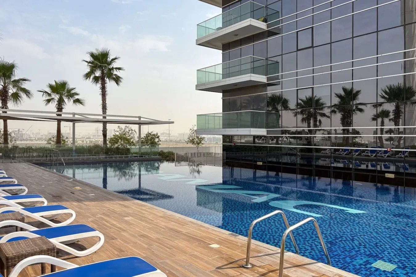 Una piscina al aire libre junto a un edificio moderno, con tumbonas en la terraza.