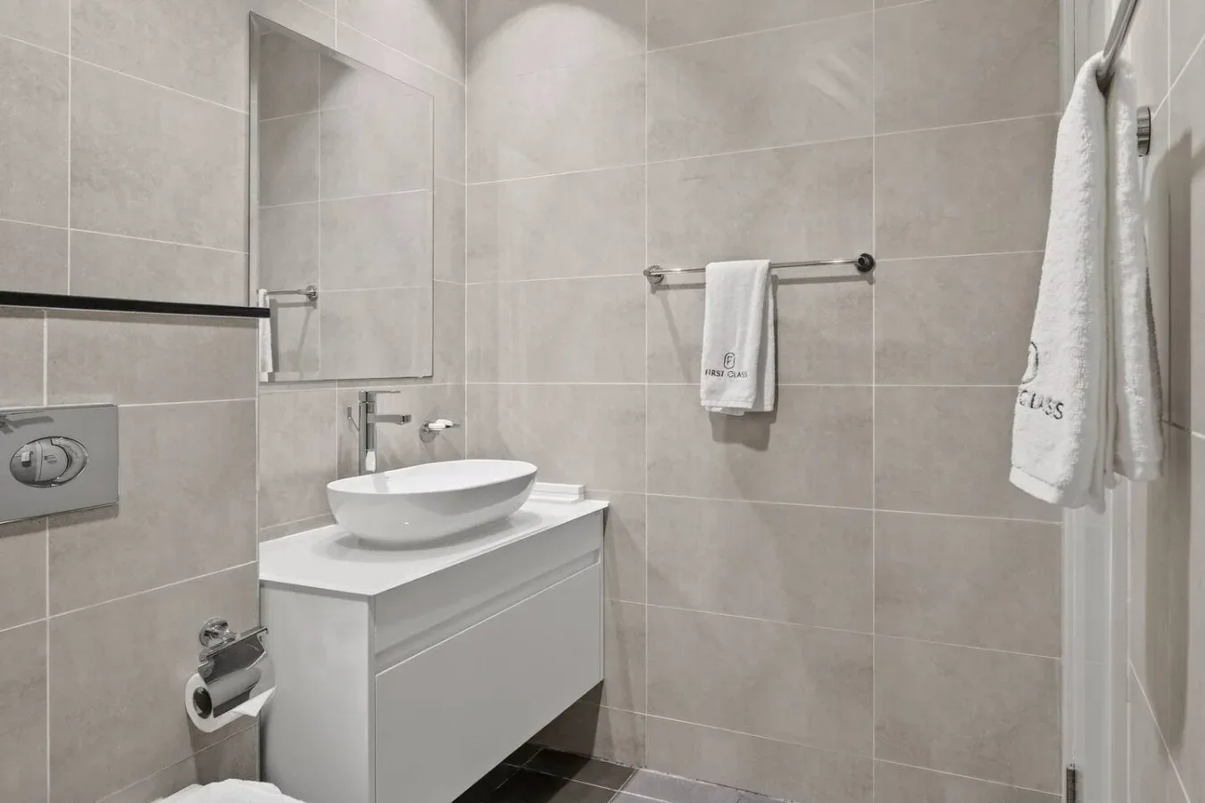 Un baño con azulejos, un lavabo sobre mueble y toallas colgadas en la pared.