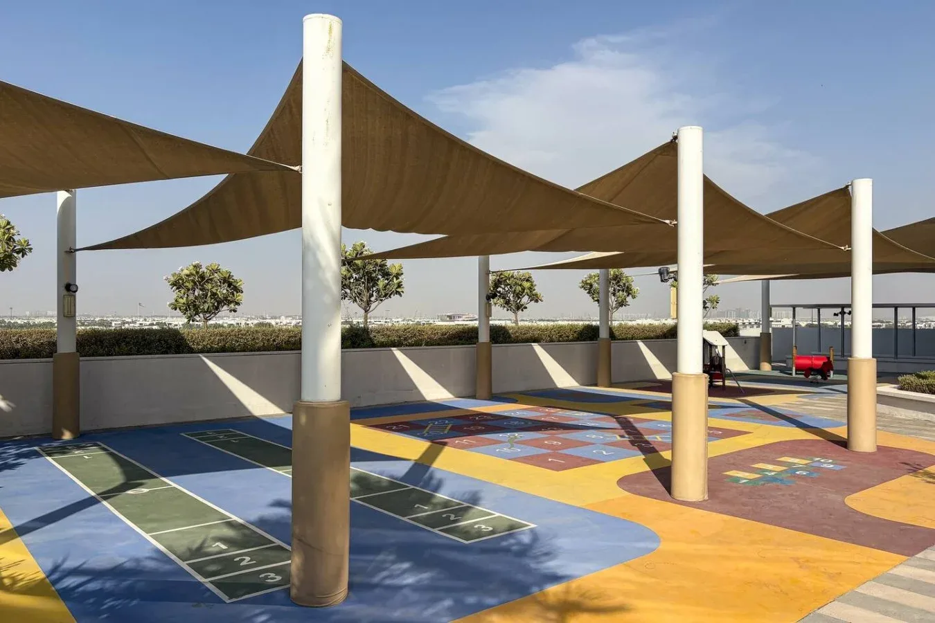 Un área de juegos al aire libre tiene un suelo pintado de colores bajo grandes toldos.