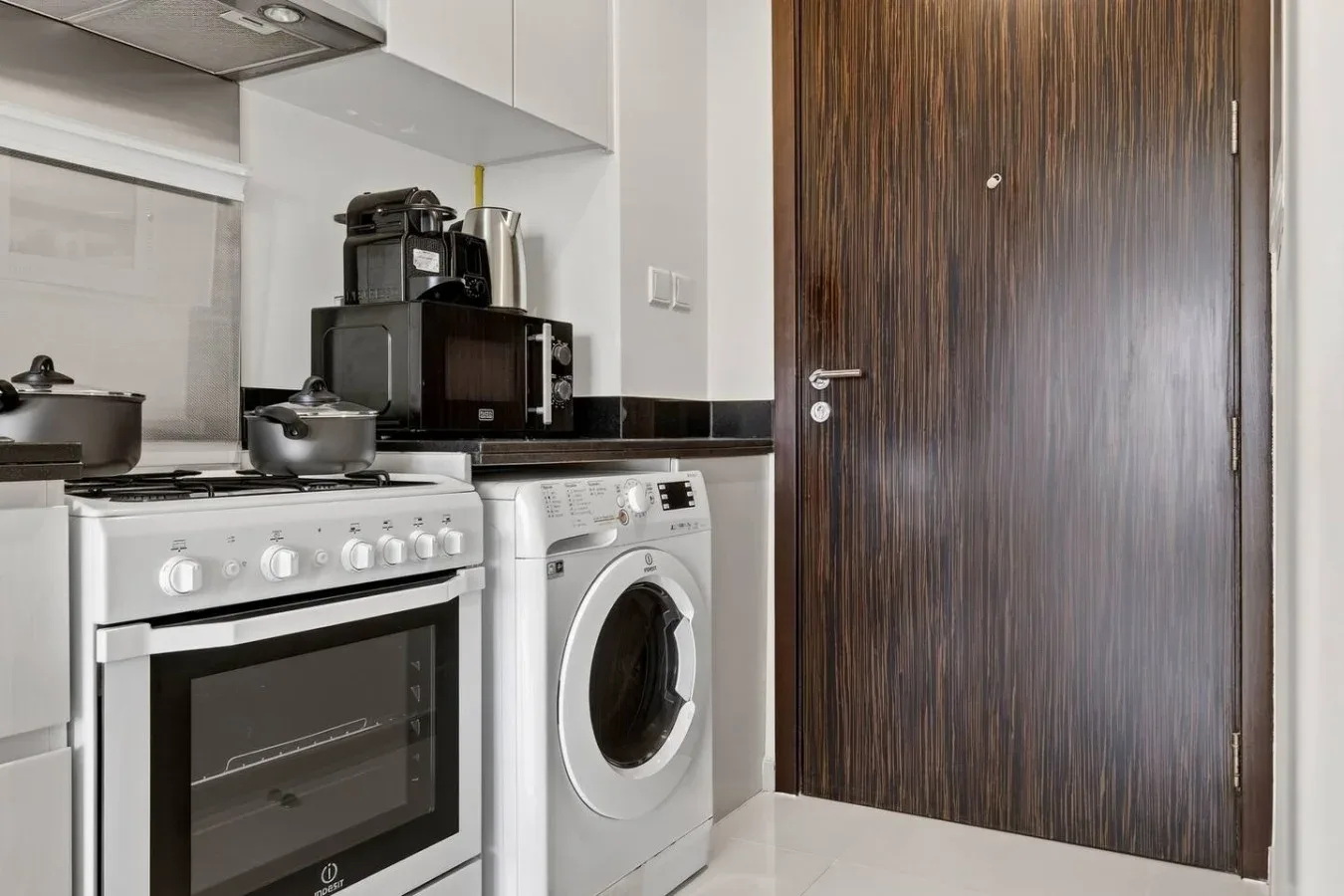 Una cocina compacta con estufa, lavadora y una puerta de madera oscura.