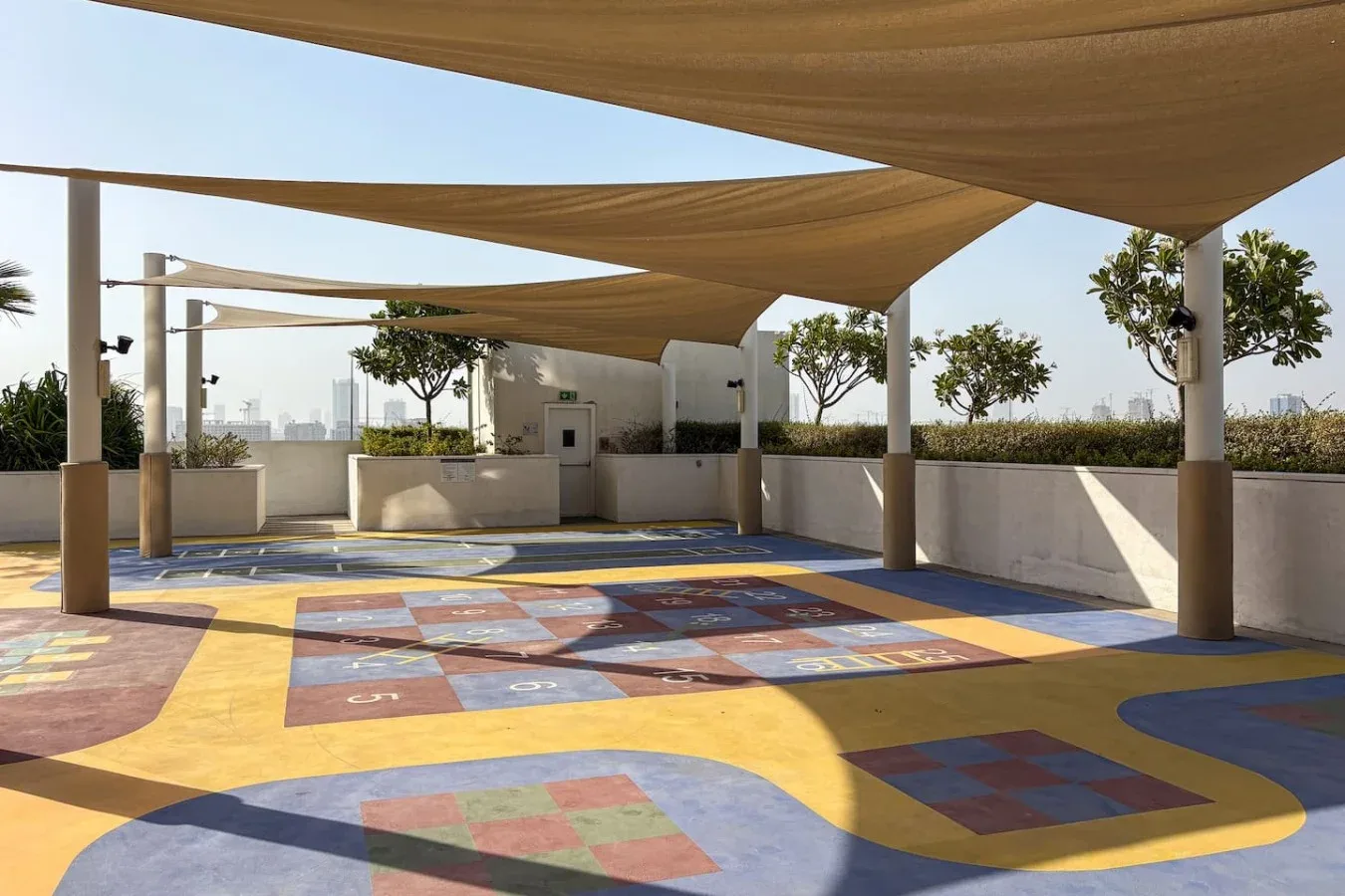 Un área recreativa al aire libre tiene juegos pintados de colores bajo grandes toldos.