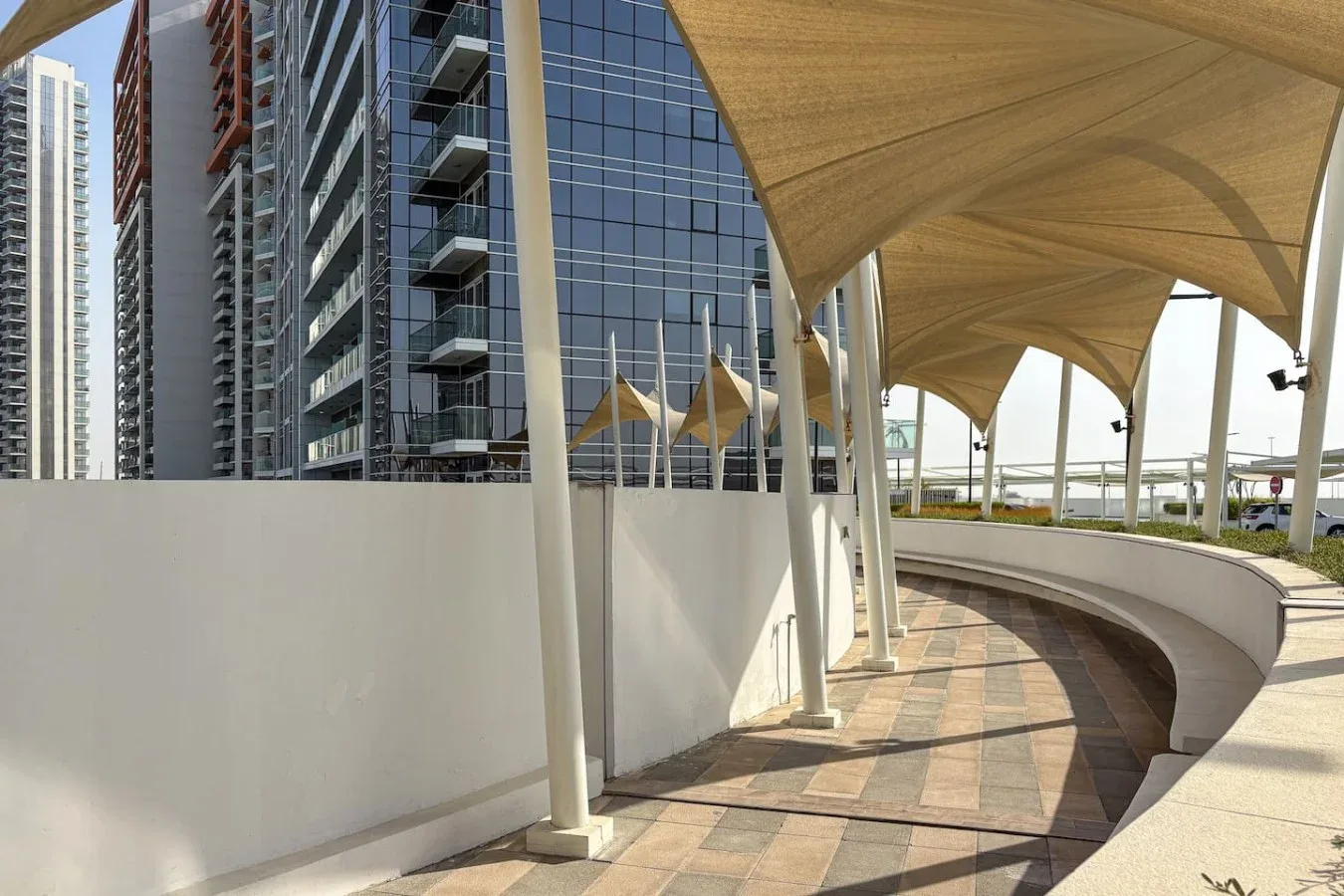 Un sendero pavimentado curvo pasa bajo varias cubiertas de tela junto a edificios modernos.