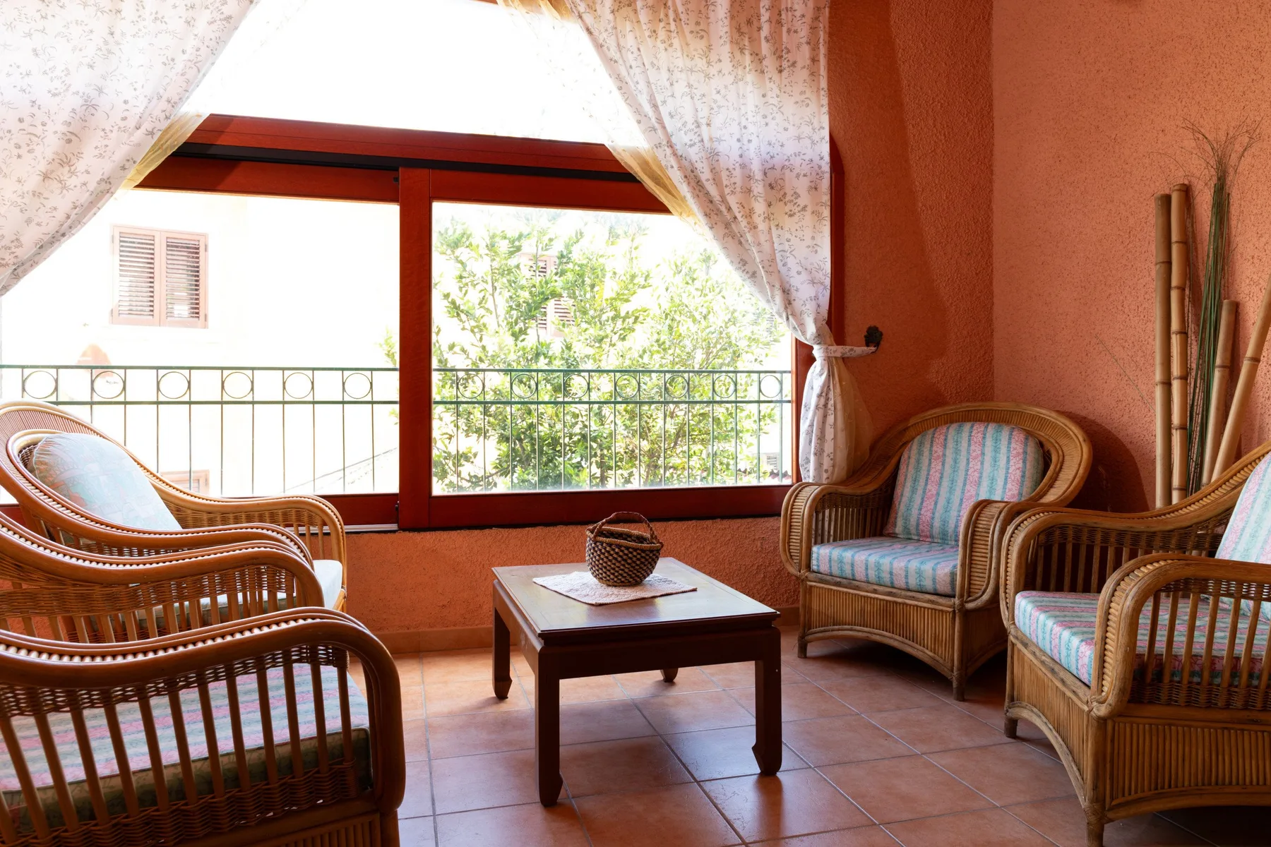 Una zona de estar con asientos de mimbre y una mesa baja junto a una ventana grande.