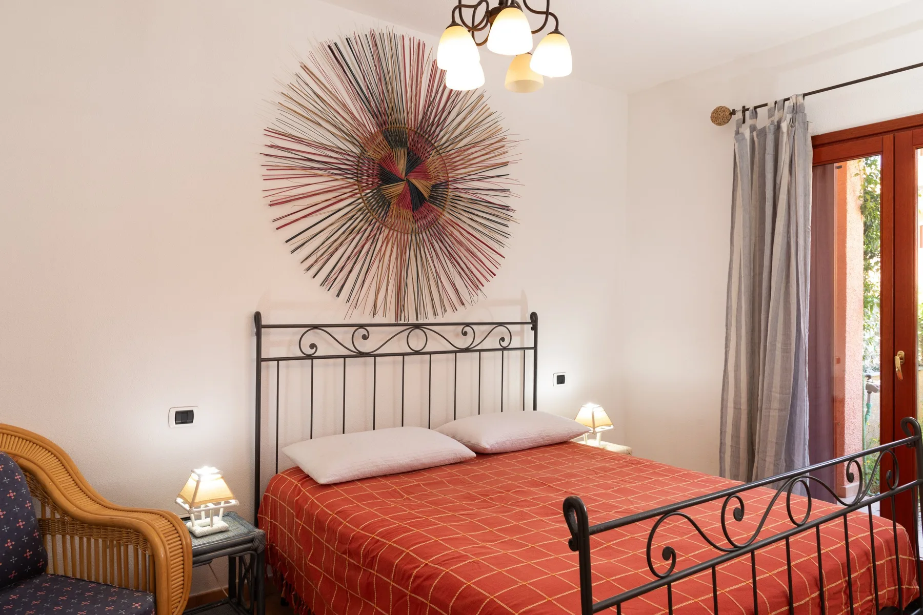 Un dormitorio con una cama de metal, ropa de cama estampada y una puerta de cristal con cortinas.