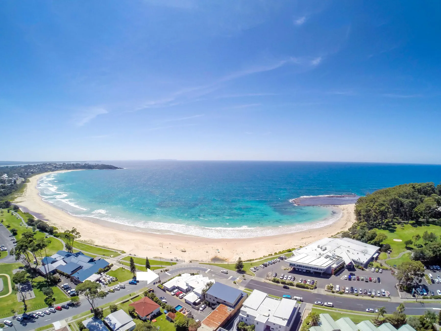 Aerial view of a curved beach and turquoise ocean beside a coastal town.