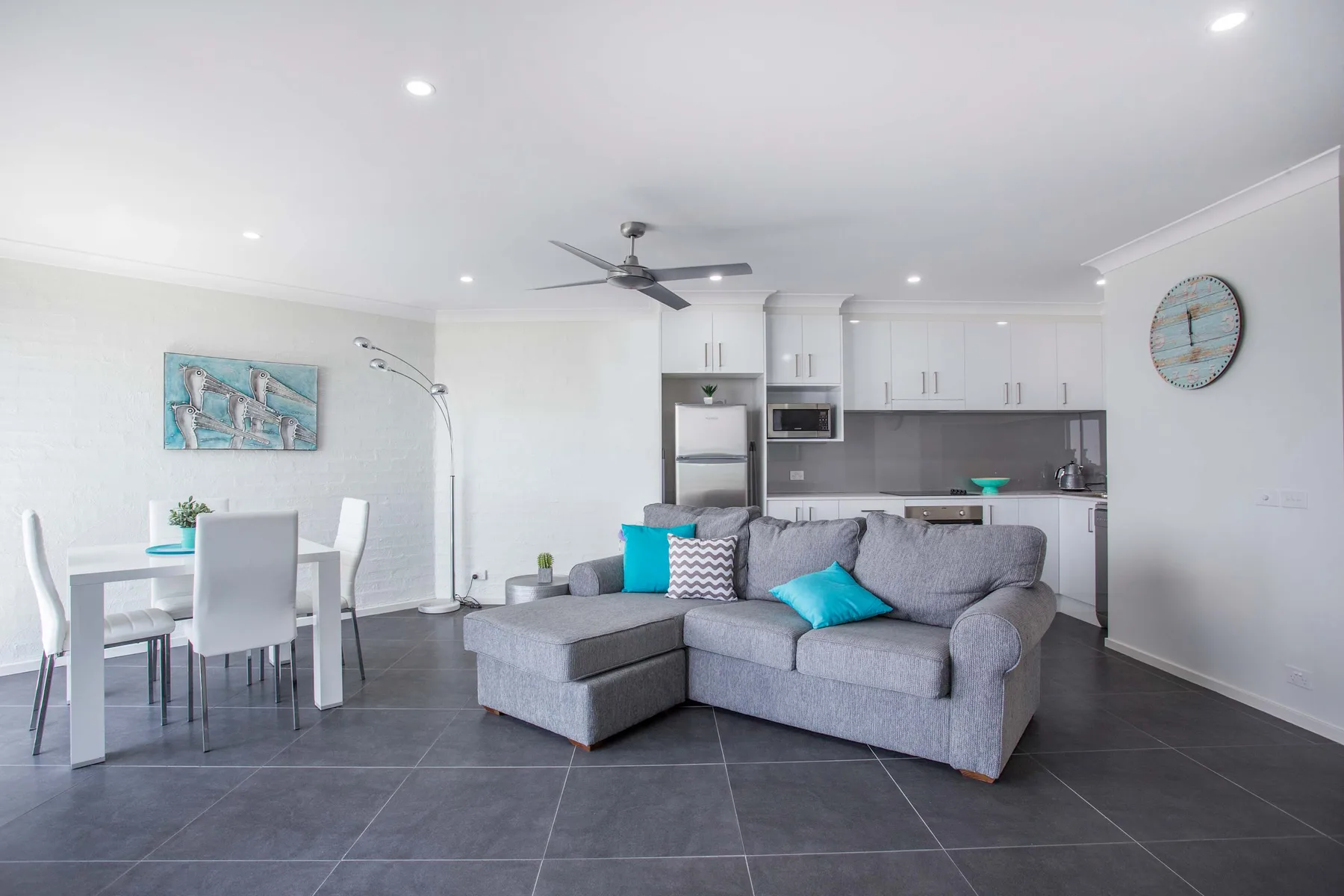Open-plan living room with gray seating, a dining table, and kitchen.