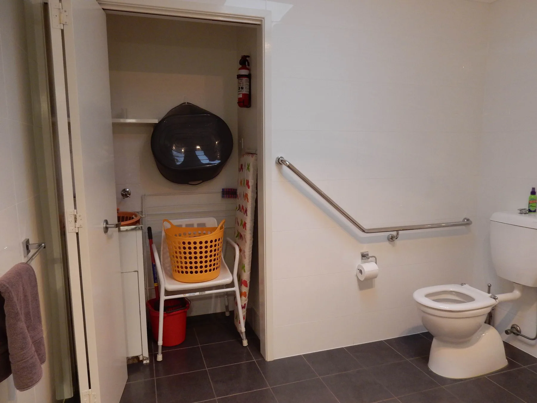 A bathroom with a toilet and a storage nook containing cleaning supplies.